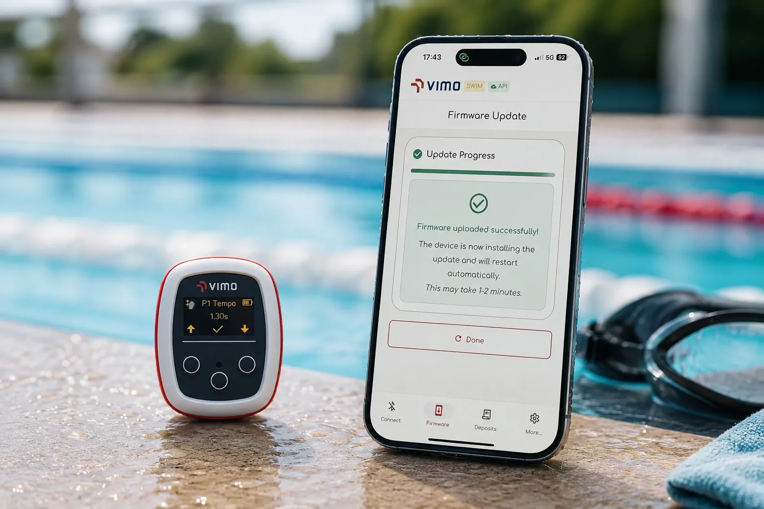 VimoSwim tempo trainer beside a phone running the VimoSwim app at a poolside, mid firmware update